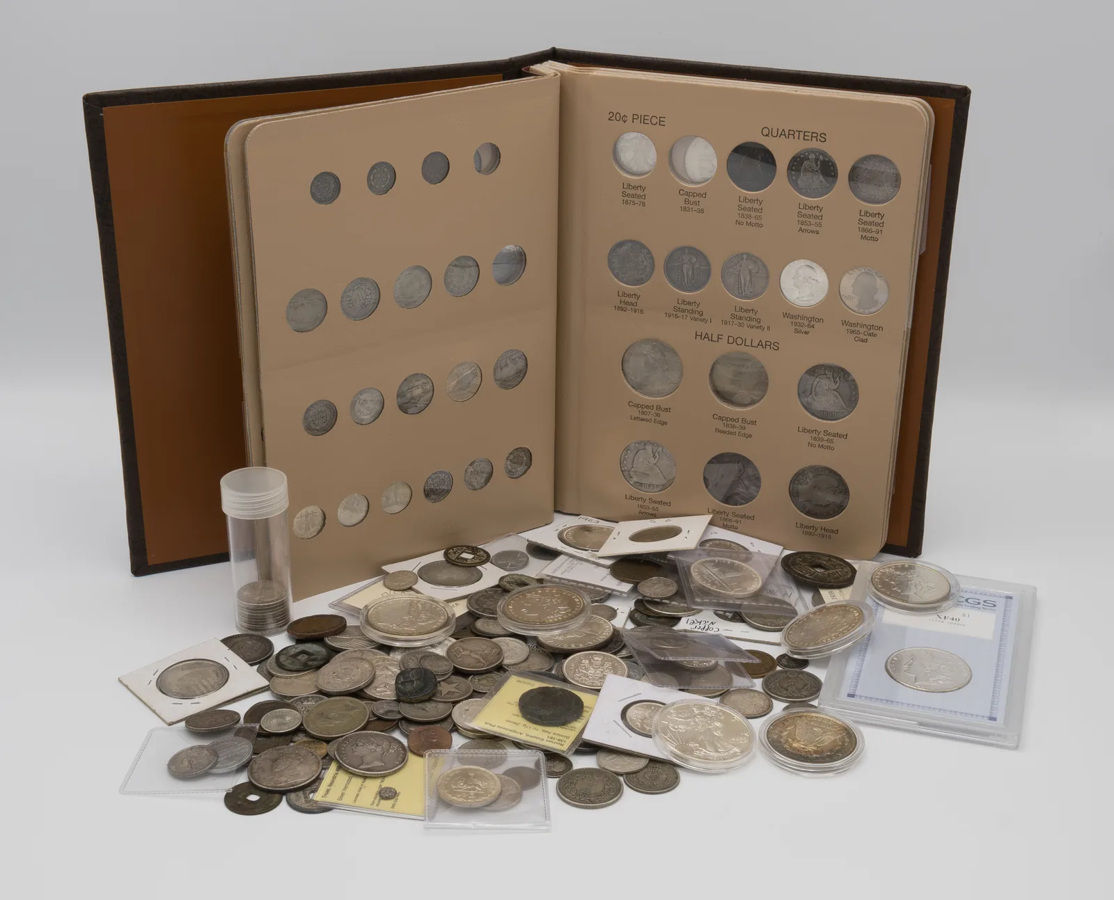 Coin album of U.S. quarters and half dollars with a pile of raw and slabbed coins in front